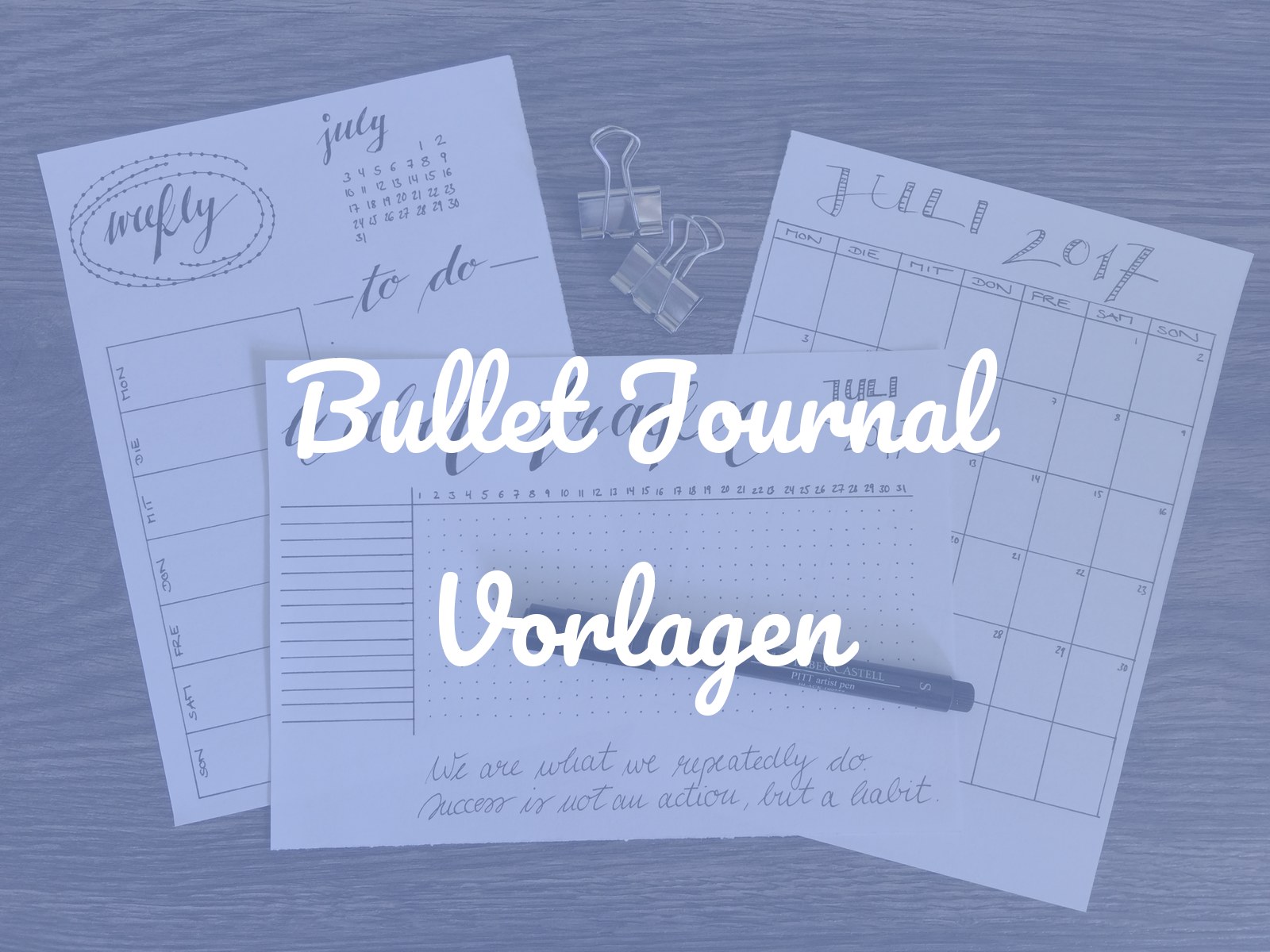 Ausgedruckte Bullet-Journal-Vorlagen für Juli auf einem Holztisch: Wochenübersicht, Habit Tracker und Monatskalender, dazu ein Fineliner und zwei Metallklammern